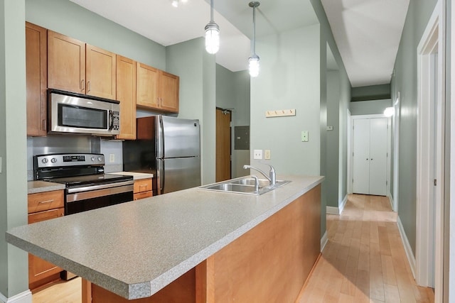 kitchen with baseboards, a sink, light wood-style floors, appliances with stainless steel finishes, and pendant lighting