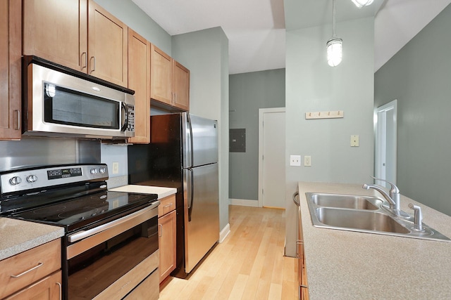 kitchen with a sink, stainless steel appliances, light wood-style floors, light countertops, and hanging light fixtures