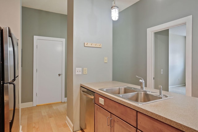 kitchen with light wood finished floors, pendant lighting, light countertops, appliances with stainless steel finishes, and a sink