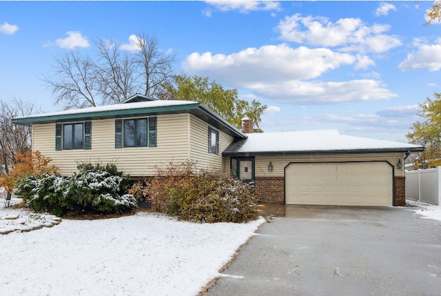 split level home featuring fence, driveway, a chimney, a garage, and brick siding