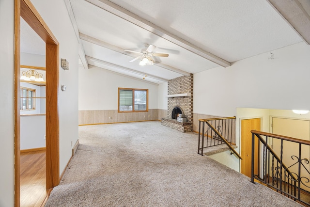 carpeted living room featuring a wainscoted wall, lofted ceiling with beams, a fireplace, ceiling fan, and a textured ceiling