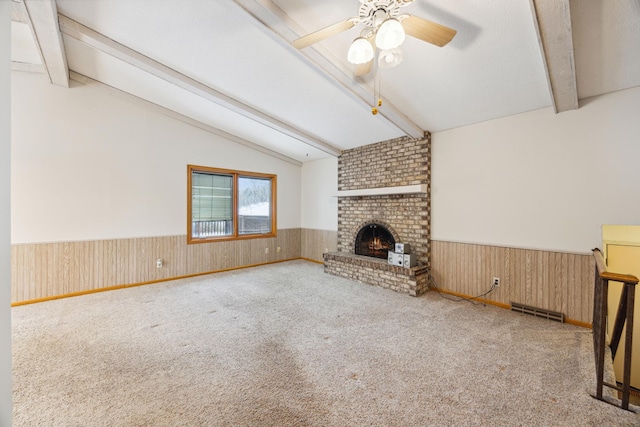 unfurnished living room with a wainscoted wall, a brick fireplace, vaulted ceiling with beams, and visible vents