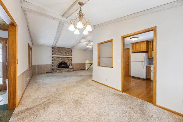 unfurnished living room featuring a wainscoted wall, light carpet, beamed ceiling, and a fireplace