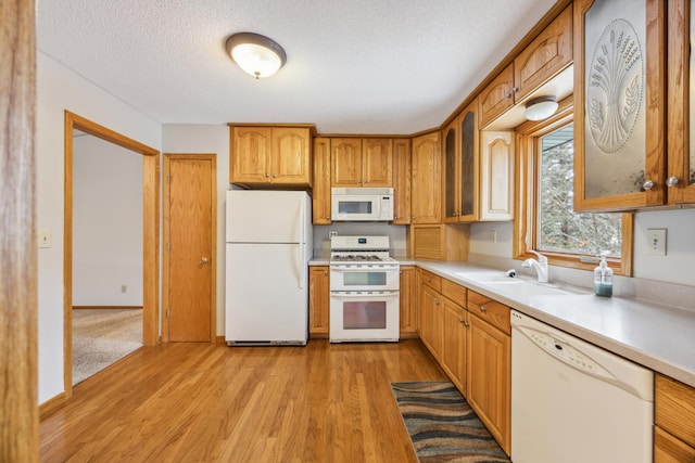 kitchen with light wood finished floors, white appliances, light countertops, and a sink