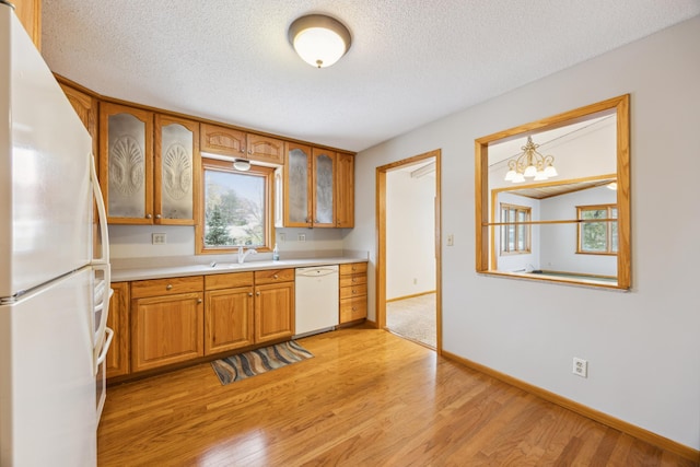 kitchen featuring light wood-type flooring, light countertops, brown cabinetry, white appliances, and a sink