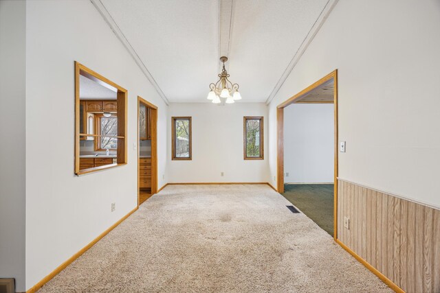 unfurnished room with visible vents, ornamental molding, carpet floors, wooden walls, and a chandelier