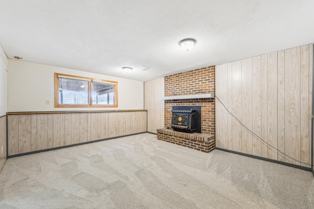 unfurnished living room featuring a wainscoted wall, a textured ceiling, carpet, wood walls, and a wood stove