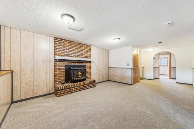 unfurnished living room featuring visible vents, carpet, wood walls, arched walkways, and a textured ceiling