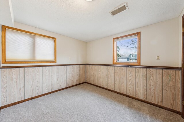 unfurnished room with visible vents, a textured ceiling, carpet, and a wainscoted wall