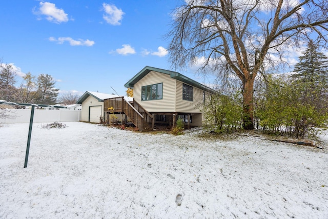 snow covered rear of property with stairs, a garage, and fence