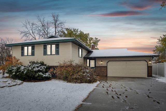 tri-level home with aphalt driveway, brick siding, a garage, and fence