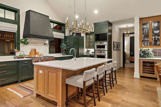 kitchen featuring an inviting chandelier, wine cooler, wall chimney range hood, light countertops, and green cabinetry