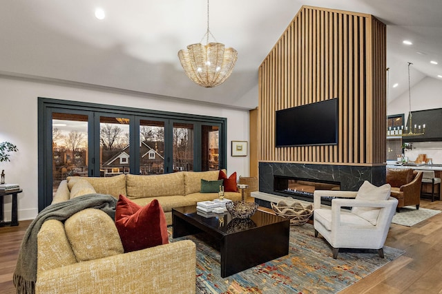 living room with a chandelier, recessed lighting, wood finished floors, lofted ceiling, and a high end fireplace