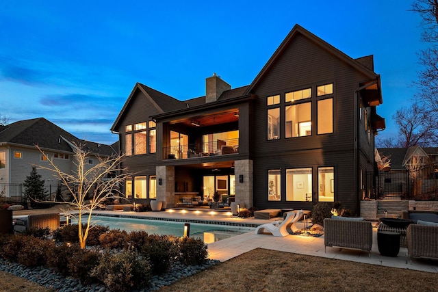 back of house at dusk featuring a chimney, an outdoor pool, a balcony, an outdoor hangout area, and a patio
