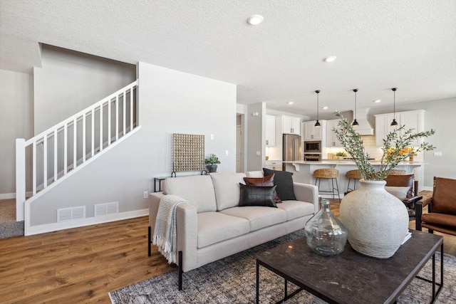 living room featuring a textured ceiling, stairs, baseboards, and wood finished floors