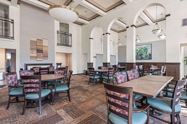 dining space featuring visible vents, wainscoting, coffered ceiling, and a towering ceiling