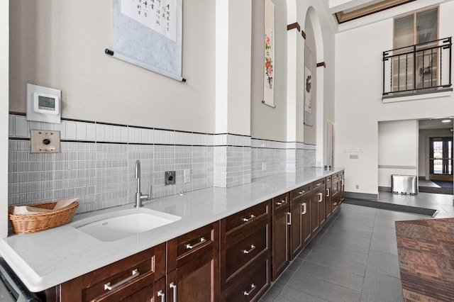 kitchen with a sink, light stone counters, dark brown cabinets, and dark tile patterned floors