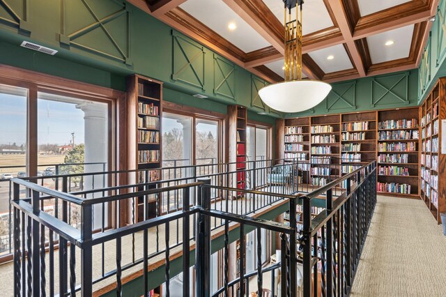 hall featuring beam ceiling, an upstairs landing, coffered ceiling, and light carpet