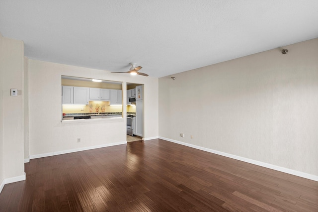 unfurnished living room with baseboards, dark wood-type flooring, a ceiling fan, and a sink