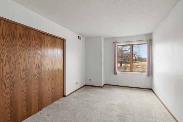 spare room featuring light carpet, visible vents, a textured ceiling, and baseboards