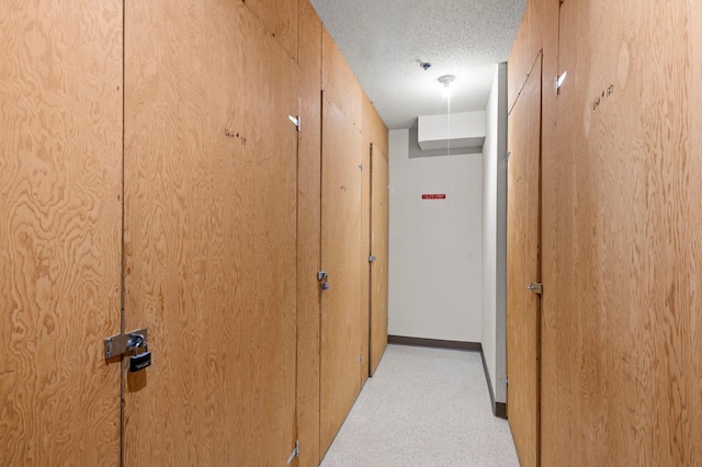 corridor featuring carpet flooring, a textured ceiling, and baseboards