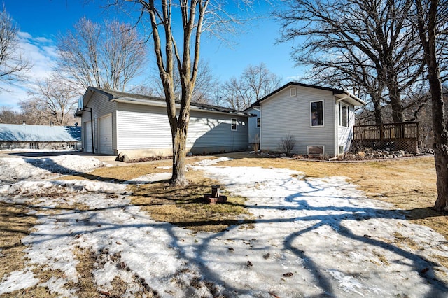 view of snow covered exterior featuring a garage, an outbuilding, a deck, and fence