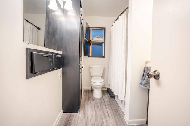 full bathroom featuring curtained shower, toilet, baseboards, and wood finished floors