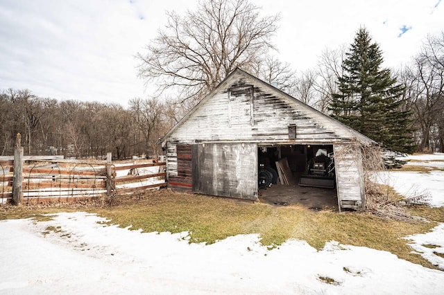 snow covered structure featuring an outbuilding and fence