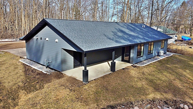 view of side of home with a patio area, a lawn, and roof with shingles