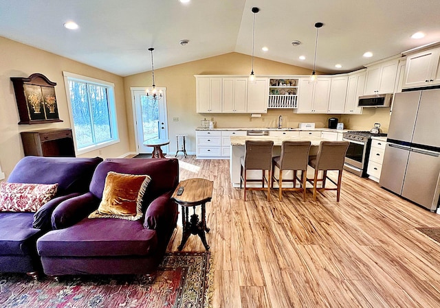 kitchen featuring a kitchen bar, open floor plan, appliances with stainless steel finishes, light wood finished floors, and lofted ceiling