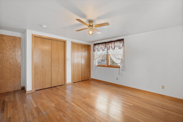 unfurnished bedroom featuring baseboards, multiple closets, light wood-style floors, and ceiling fan