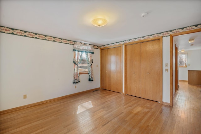 unfurnished bedroom with visible vents, baseboards, light wood-type flooring, and multiple closets