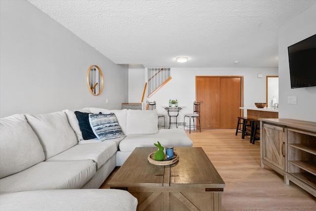 living room with stairs, light wood-style floors, and a textured ceiling