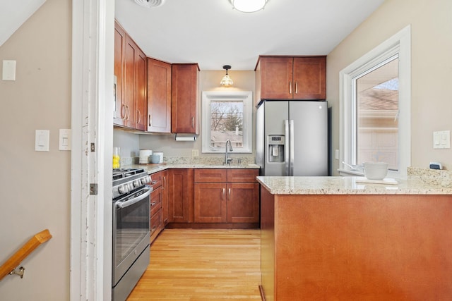 kitchen with light stone counters, a peninsula, a sink, stainless steel appliances, and light wood-type flooring