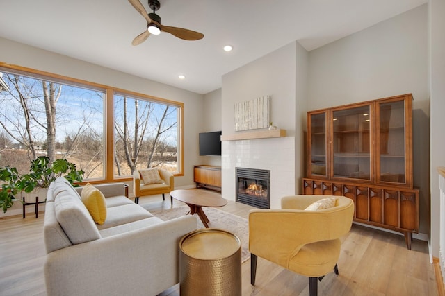 living room with a tiled fireplace, recessed lighting, light wood finished floors, baseboards, and ceiling fan