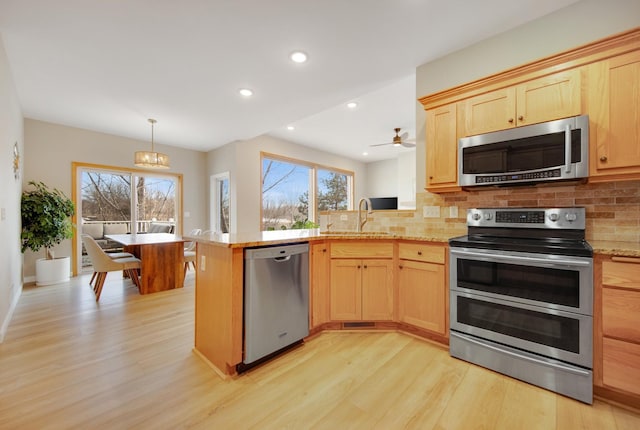 kitchen with light brown cabinetry, a sink, stainless steel appliances, a peninsula, and light wood finished floors