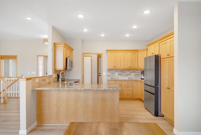 kitchen featuring light brown cabinets, a peninsula, light wood-style flooring, a sink, and appliances with stainless steel finishes