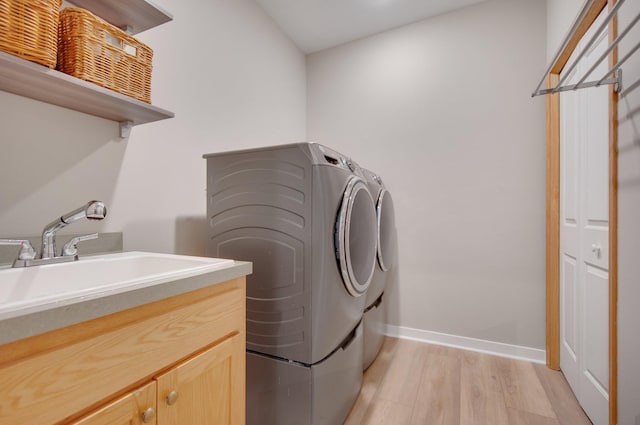 laundry room with light wood-type flooring, independent washer and dryer, a sink, cabinet space, and baseboards