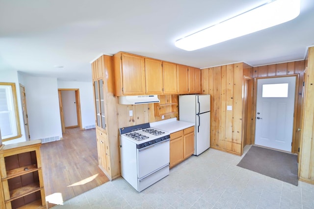 kitchen with visible vents, light floors, wood walls, range hood, and white appliances