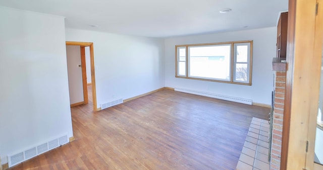 unfurnished room featuring baseboards, wood finished floors, visible vents, and a baseboard radiator