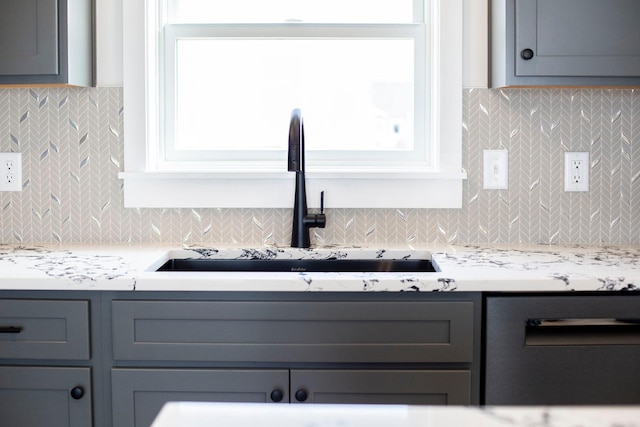 kitchen featuring gray cabinetry, a sink, light countertops, stainless steel dishwasher, and tasteful backsplash