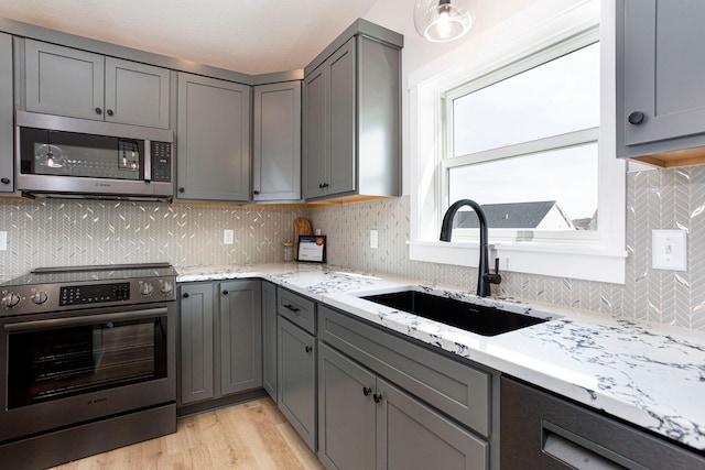 kitchen with light stone countertops, a sink, gray cabinetry, stainless steel appliances, and tasteful backsplash