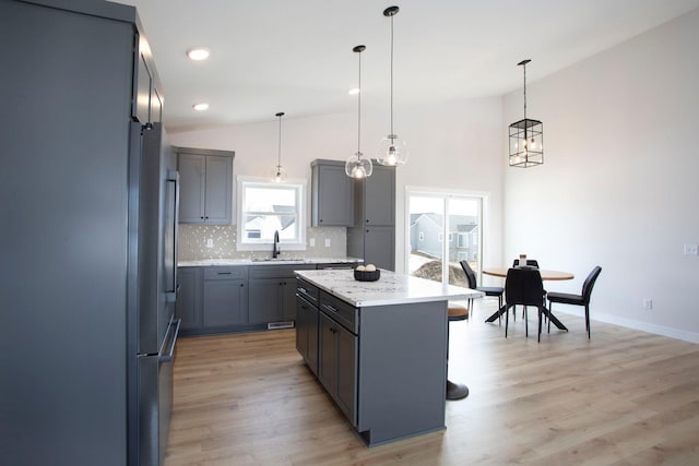 kitchen featuring light wood finished floors, backsplash, gray cabinetry, lofted ceiling, and a sink