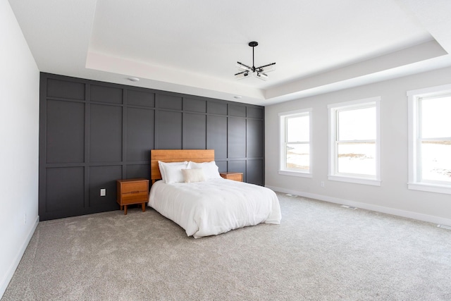 carpeted bedroom featuring a notable chandelier, a decorative wall, baseboards, and a tray ceiling