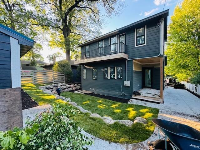 back of house featuring a balcony, a lawn, and fence