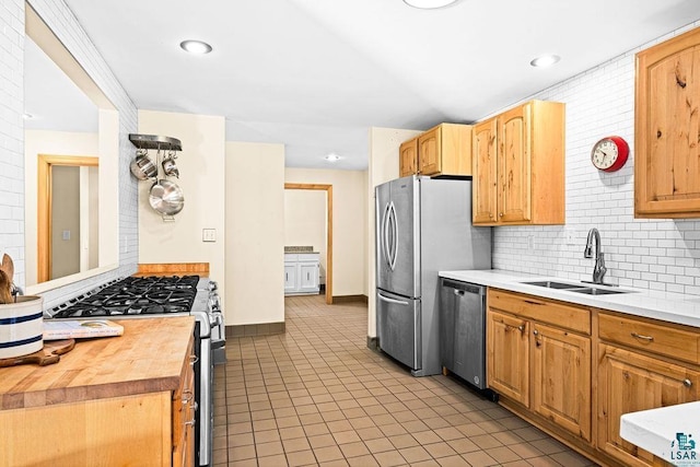 kitchen with butcher block countertops, a sink, backsplash, stainless steel appliances, and light tile patterned flooring