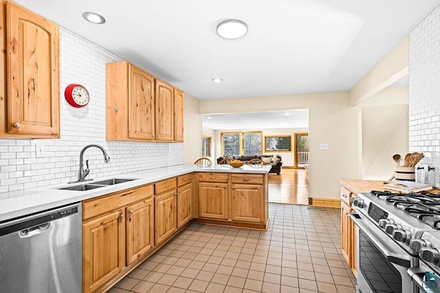 kitchen featuring a sink, stainless steel appliances, a peninsula, light countertops, and decorative backsplash