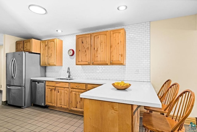 kitchen with a sink, stainless steel appliances, a peninsula, light countertops, and decorative backsplash