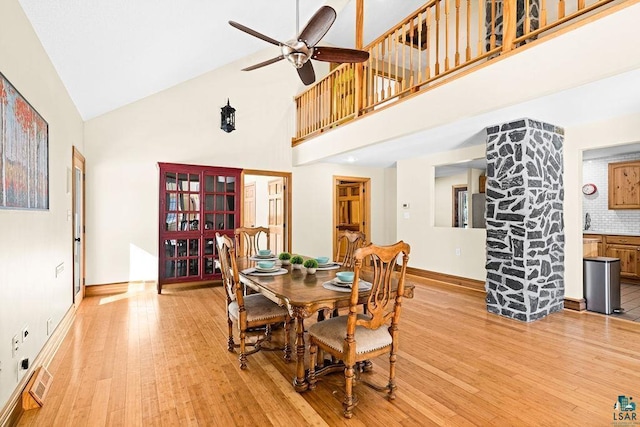 dining area featuring a ceiling fan, visible vents, light wood finished floors, baseboards, and a towering ceiling