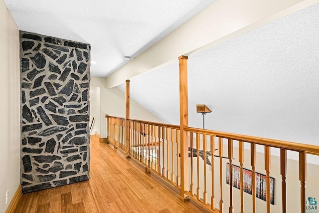 hall with lofted ceiling with beams, a textured ceiling, and wood finished floors